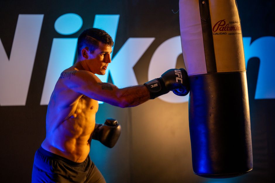 A male boxer trains intensely with a punching bag indoors at a gym in Mexico City.