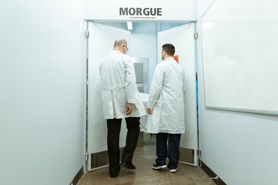 Medical professionals in lab coats entering a morgue with a body on stretcher.