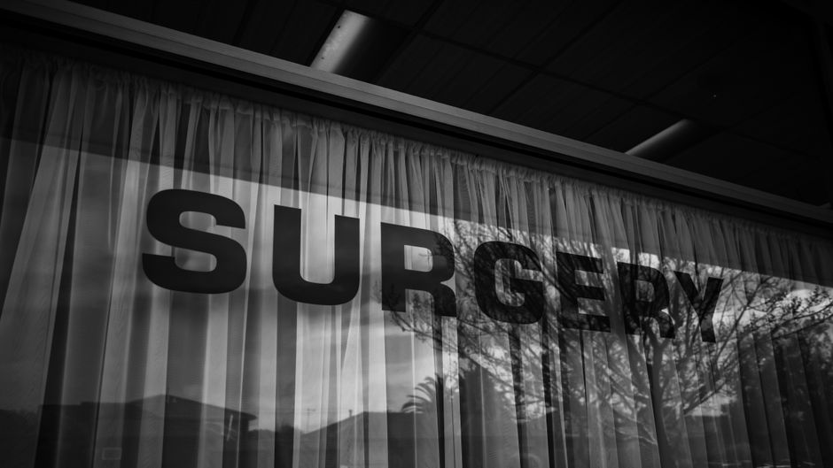 Monochrome image of a surgery sign with curtains and reflections.