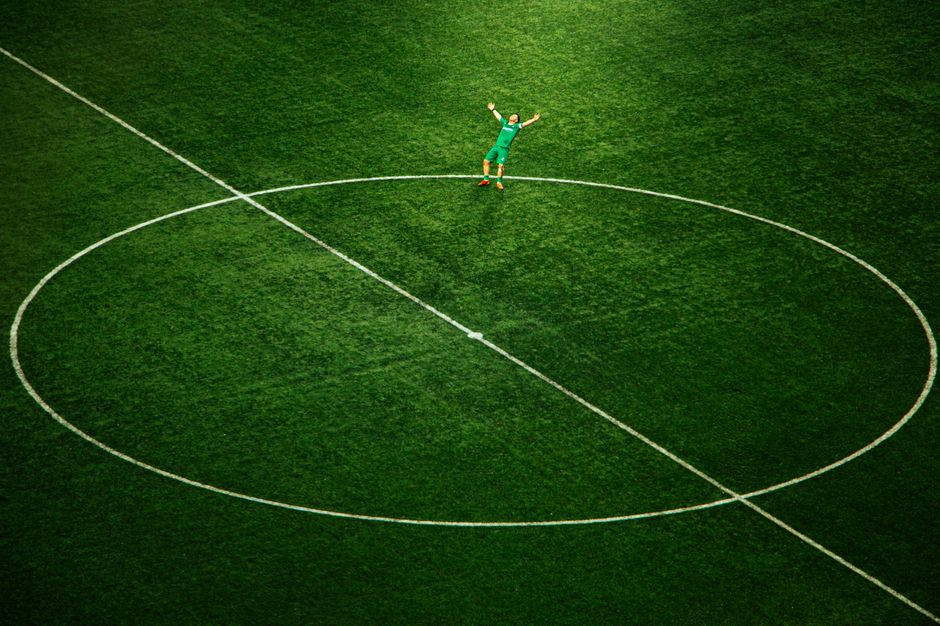 A soccer player celebrates on an empty field, spotlighted in the stadium's center circle.