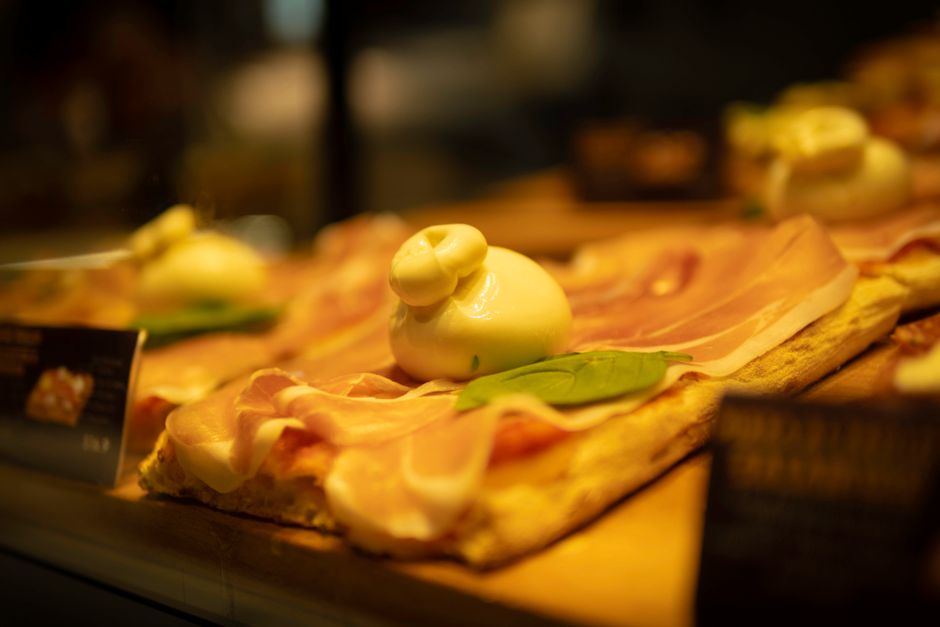Close-up of a gourmet pizza topped with prosciutto, burrata cheese, and basil leaf.