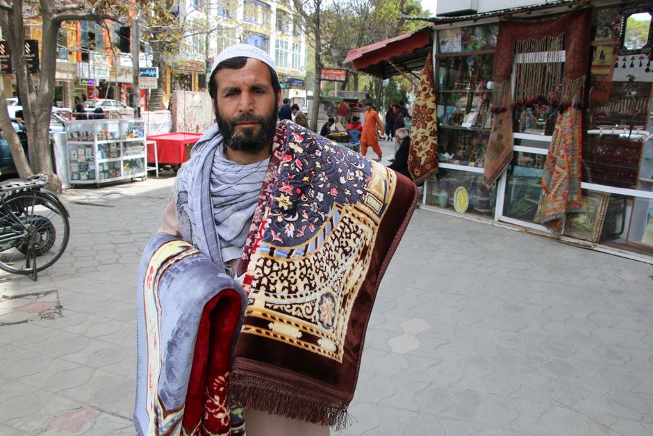 Merchant in Kabul displaying colorful rugs in outdoor market.