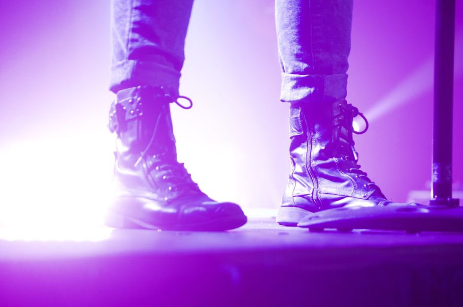 Close-up of stylish boots on stage under dramatic purple lighting at night.