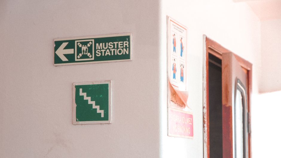 Emergency muster station signs indoors with directional and safety instructions.