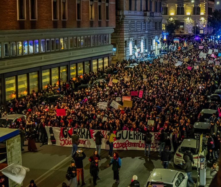 A massive nighttime protest with crowds holding banners and placards on a city street.