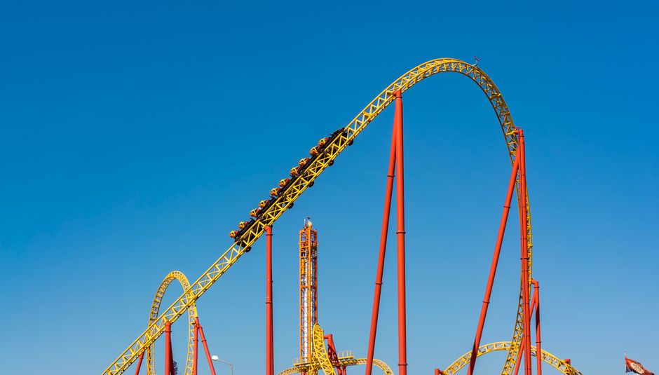 An exhilarating view of a roller coaster at an amusement park against a clear blue sky.