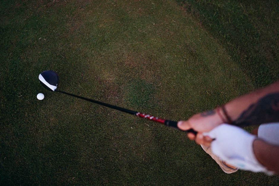 Golfer preparing to swing on a lush course, showing glove and tattoo.