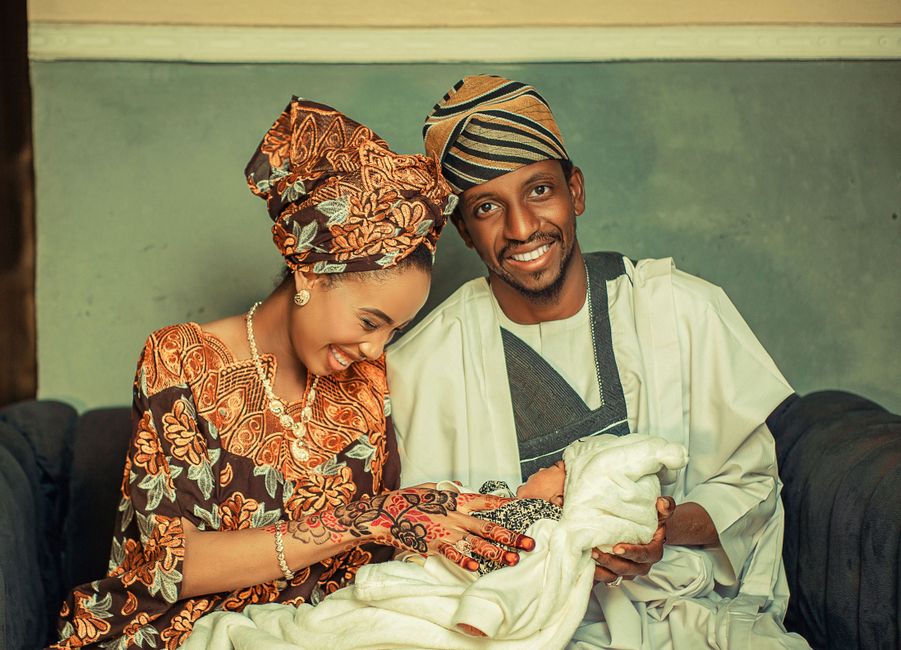 Joyful family in traditional attire holding a newborn baby, indoors.